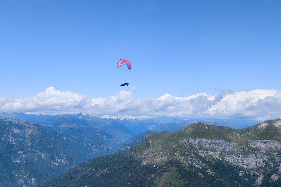 Ein einzelner Gleitschirm fliegt über Berggipfeln und einer weiten Tallandschaft