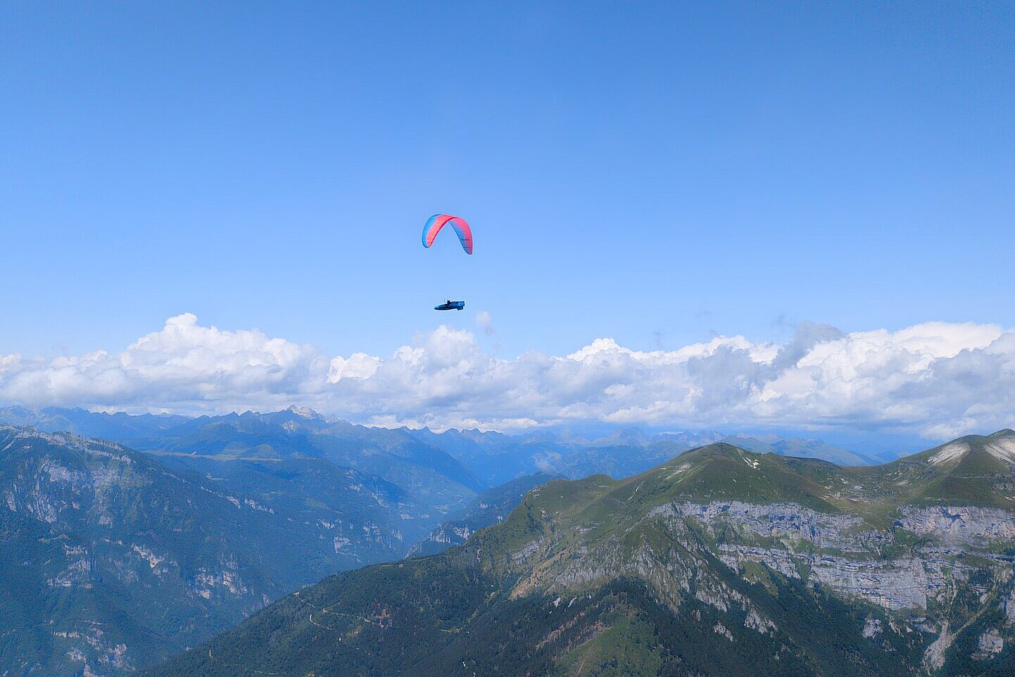 Ein einzelner Gleitschirm fliegt über Berggipfeln und einer weiten Tallandschaft