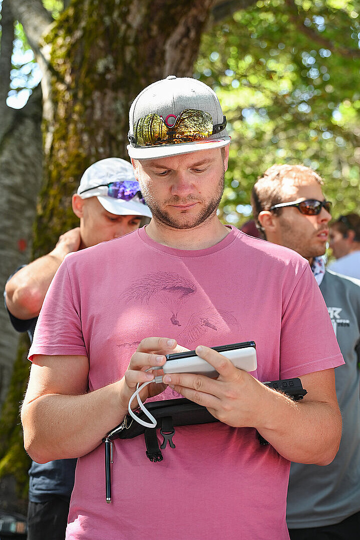 Mann in pinkem T-Shirt schaut auf ein Gerät und tippt darauf.