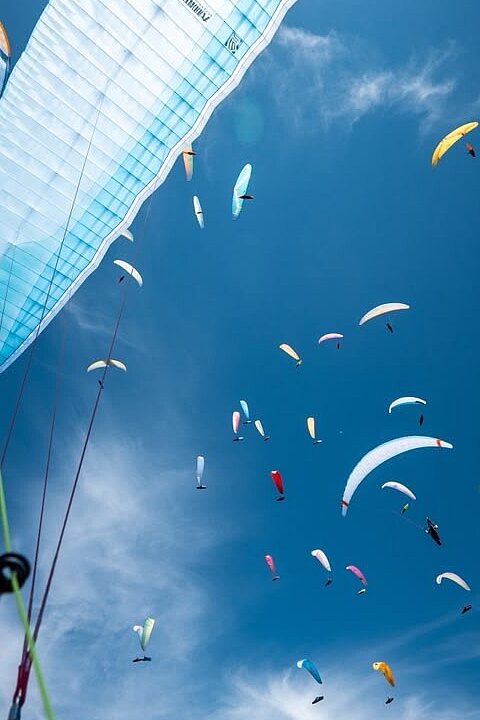 Viele Gleitschirme am blauen Himmel, im Vordergrund ein großer weißer Schirm und Leinen.