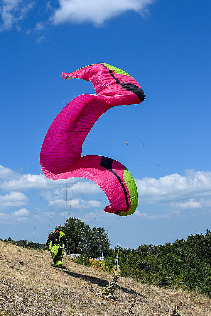 Ein pinker Gleitschirm steht über dem Startplatz, darunter läuft ein Pilot den Hang hinunter.