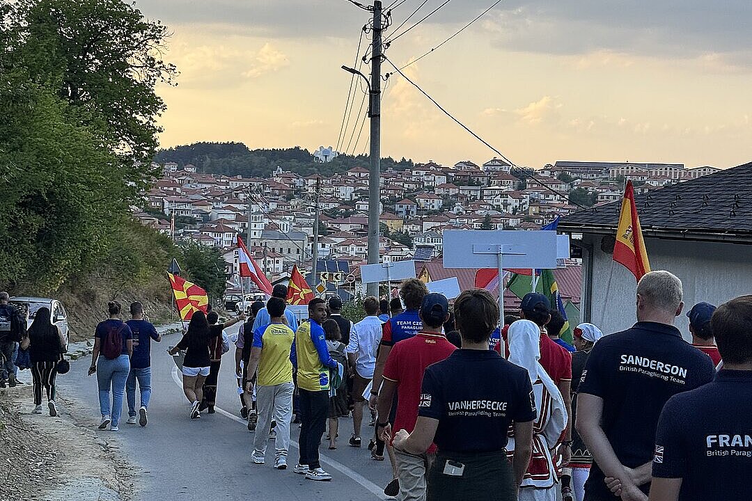 Viele Menschen mit Flaggen gehen eine Straße entlang, dahinter liegt eine Stadt im Abendlicht.