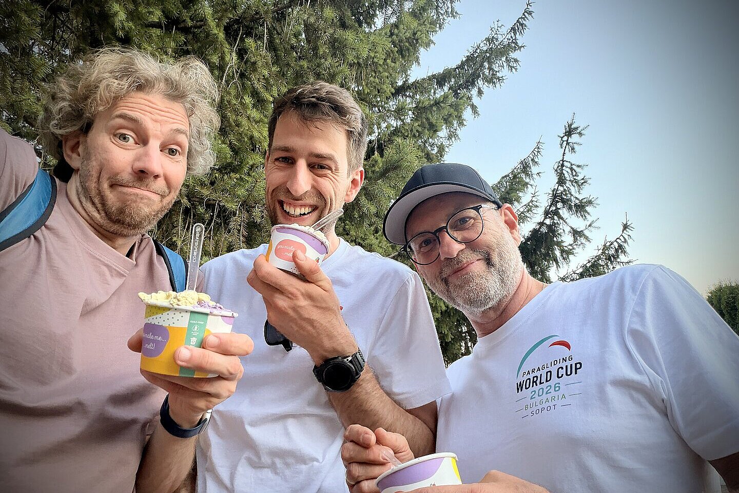 Drei Männer halten Becher mit Eis und lächeln in die Kamera.