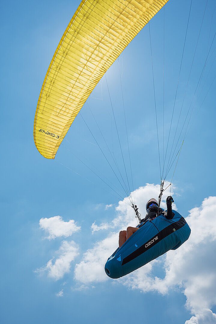 Pilot schwebt mit blauem Gurtzeug und gelbem Gleitschirm am Himmel.