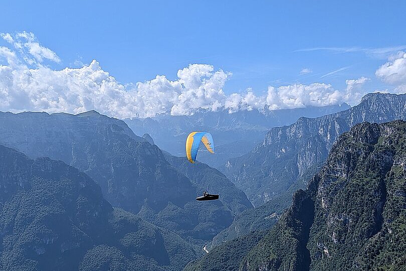 Ein Gleitschirm fliegt über eine enge Schlucht mit türkisfarbenem See und steilen Felswänden.