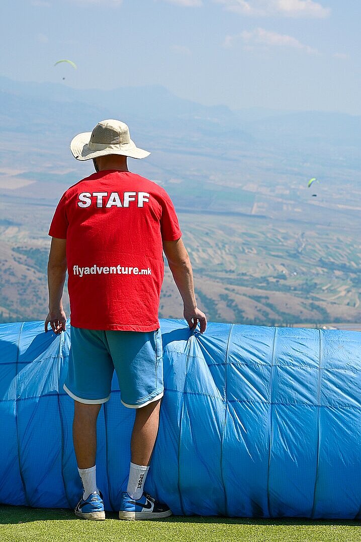 Staff-Mitglied in rotem T-Shirt steht am Hang hinter einer blauen Schutzplane.
