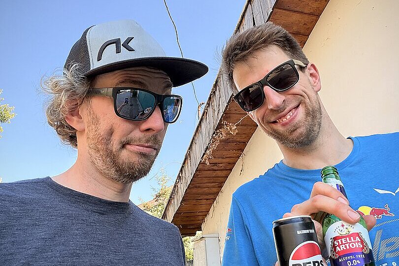 Zwei Männer mit Sonnenbrillen stehen draußen und halten eine Pepsi- und eine Bierflasche.