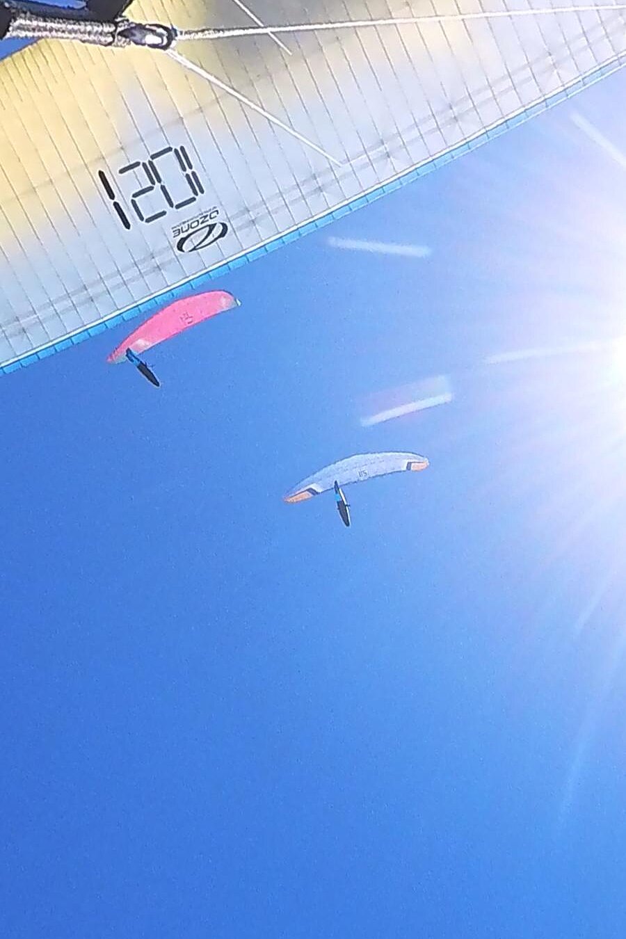 Unter einem Gleitschirm sind zwei weitere Schirme vor blauem Himmel zu sehen.