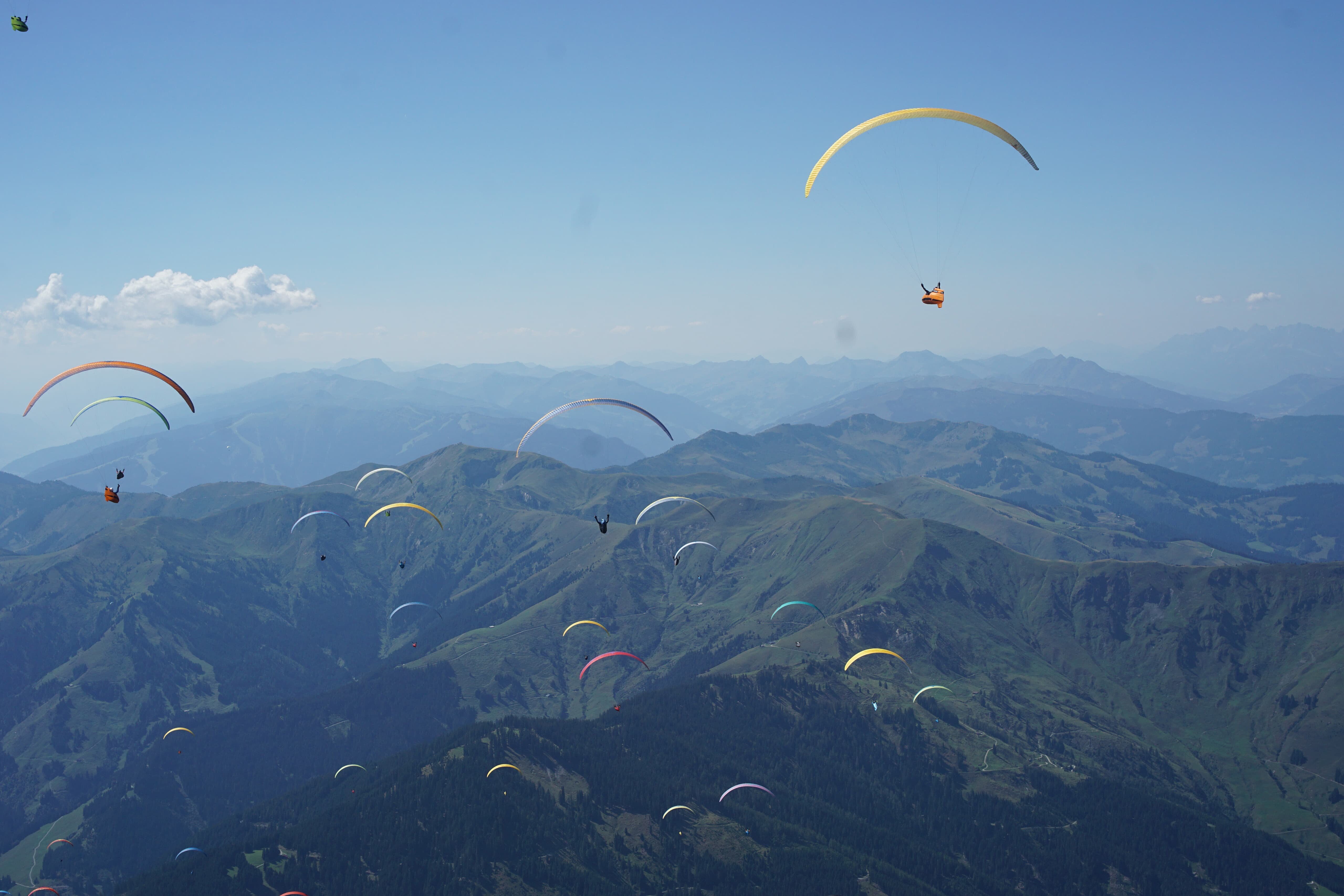 Mehrere Gleitschirme fliegen über Bergkämmen im klaren Himmel
