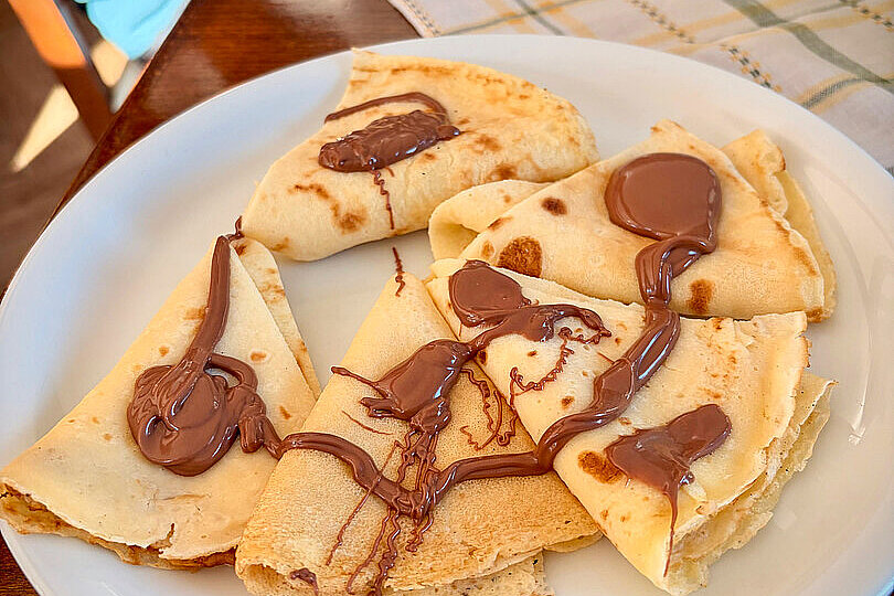 Teller mit gefalteten Crepes und Schokosoße auf einem Holztisch
