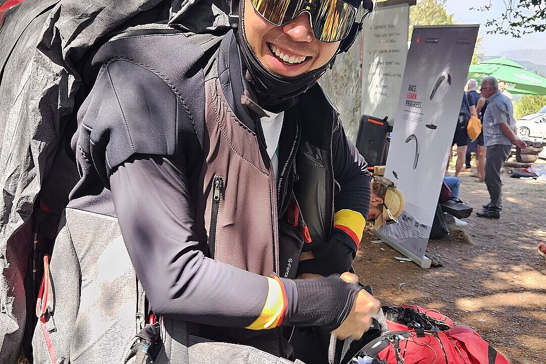 Pilot im Gurtzeug mit Helm und Sonnenbrille beim Anlegen der Ausrüstung.