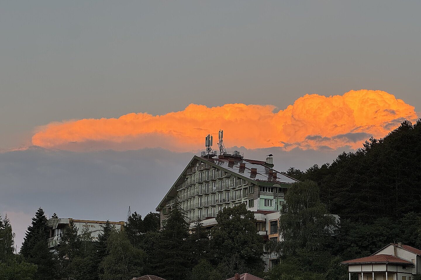 Abendhimmel über einem Hotel und Bäumen, darüber leuchtet eine orange Wolkenbank.