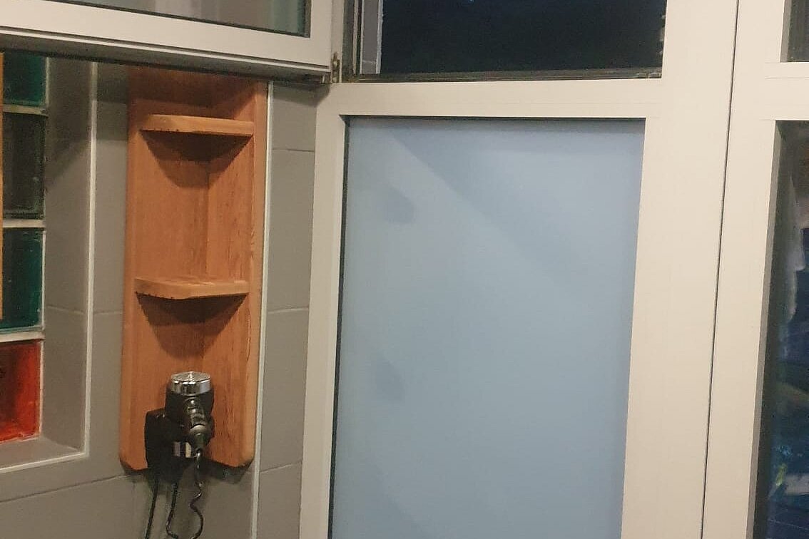 Innenraum mit offenem Fenster, Wandfliesen und einer kleinen Ablage; ein Rucksack steht unten rechts.