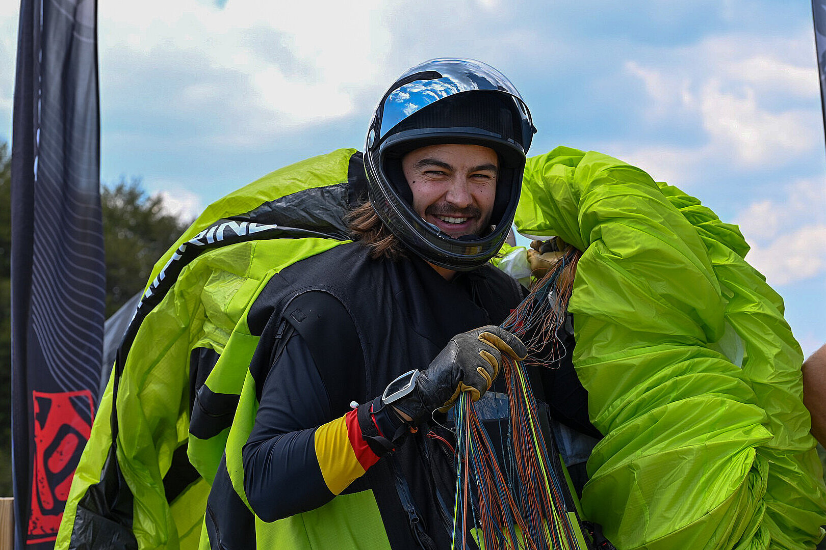 Pilot mit Helm lächelt und hält Leinen neben einem geöffneten Gleitschirm.