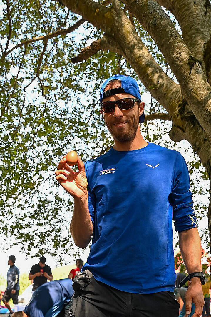 Mann mit Sonnenbrille und Kappe hält ein Ei in der Hand und lächelt.