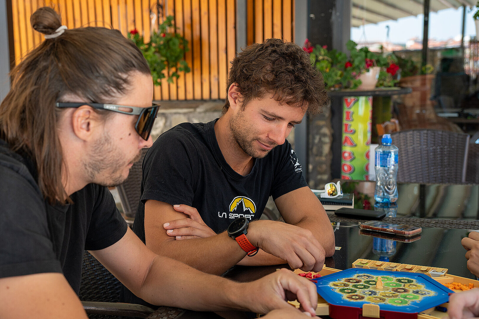Drei Personen spielen am Tisch ein Brettspiel und schauen konzentriert auf das Spielbrett