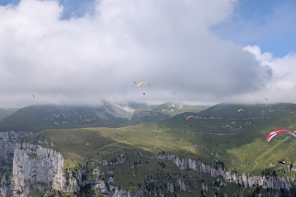 Mehrere Gleitschirme fliegen über felsigen Bergkämmen unter großen Wolken.