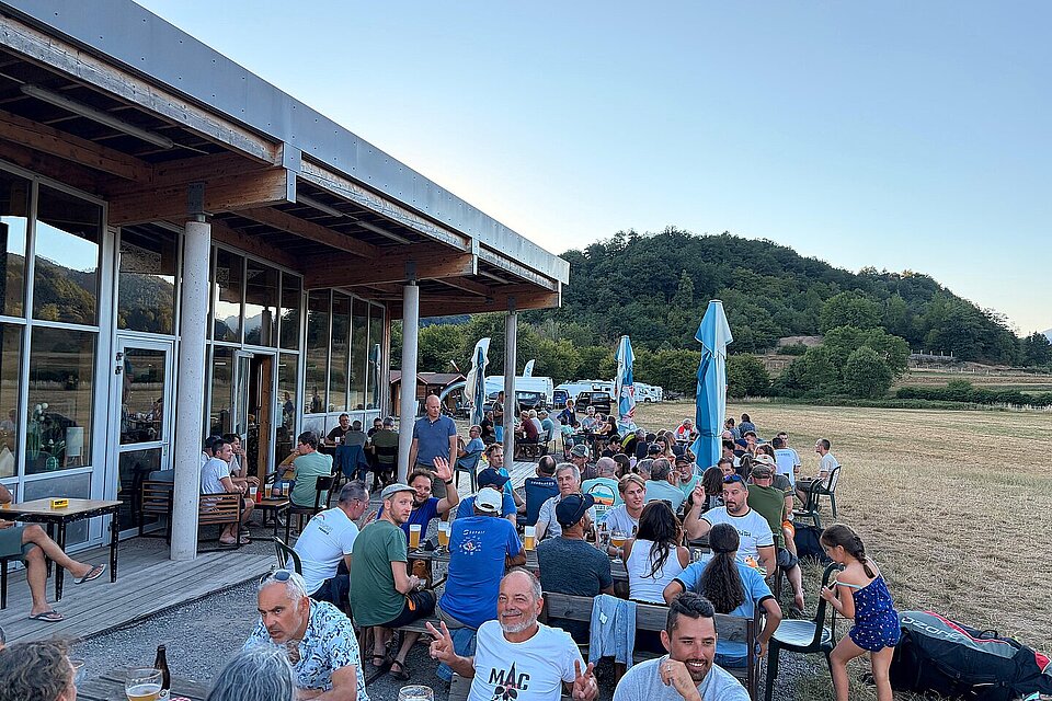 Viele Menschen sitzen draußen an Tischen vor einem Gebäude und essen und trinken.