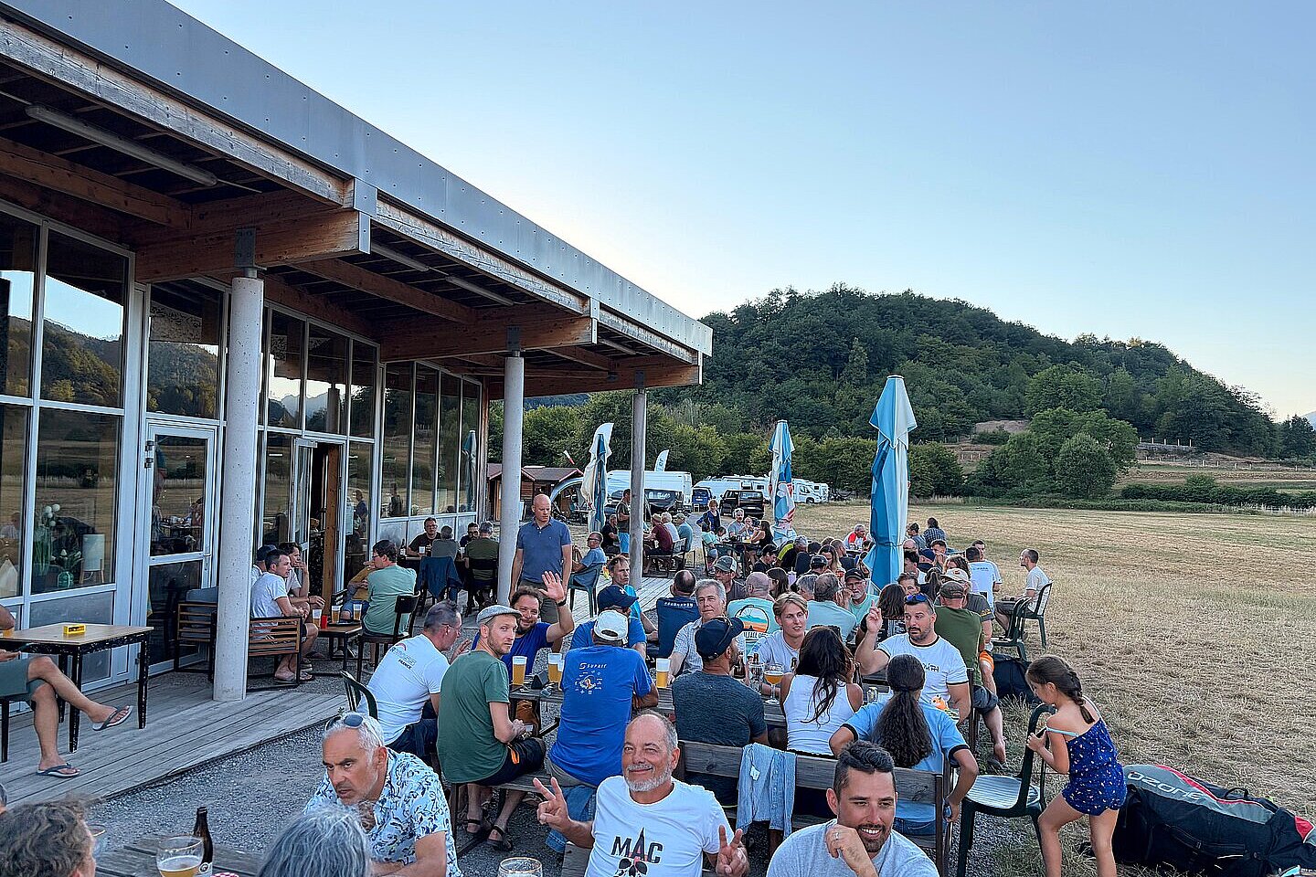 Viele Menschen sitzen draußen an Tischen vor einem Gebäude und essen und trinken.
