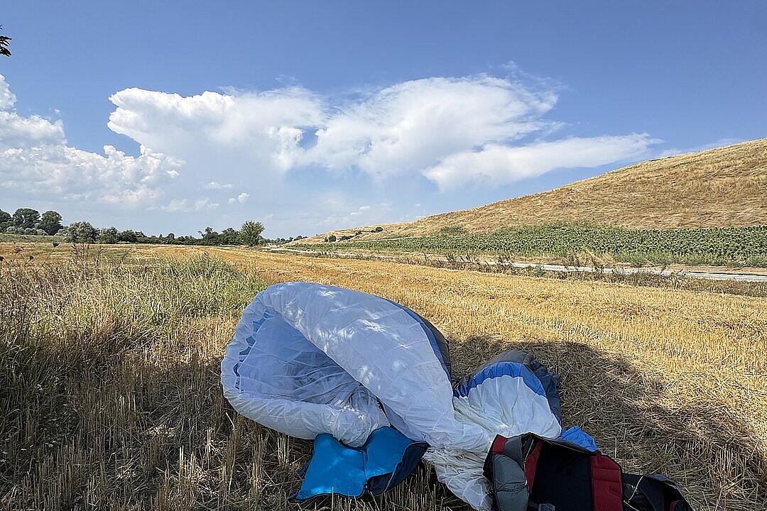 Ein leerer, halb ausgelegter Gleitschirm liegt auf trockenem Gras unter offenem Himmel.