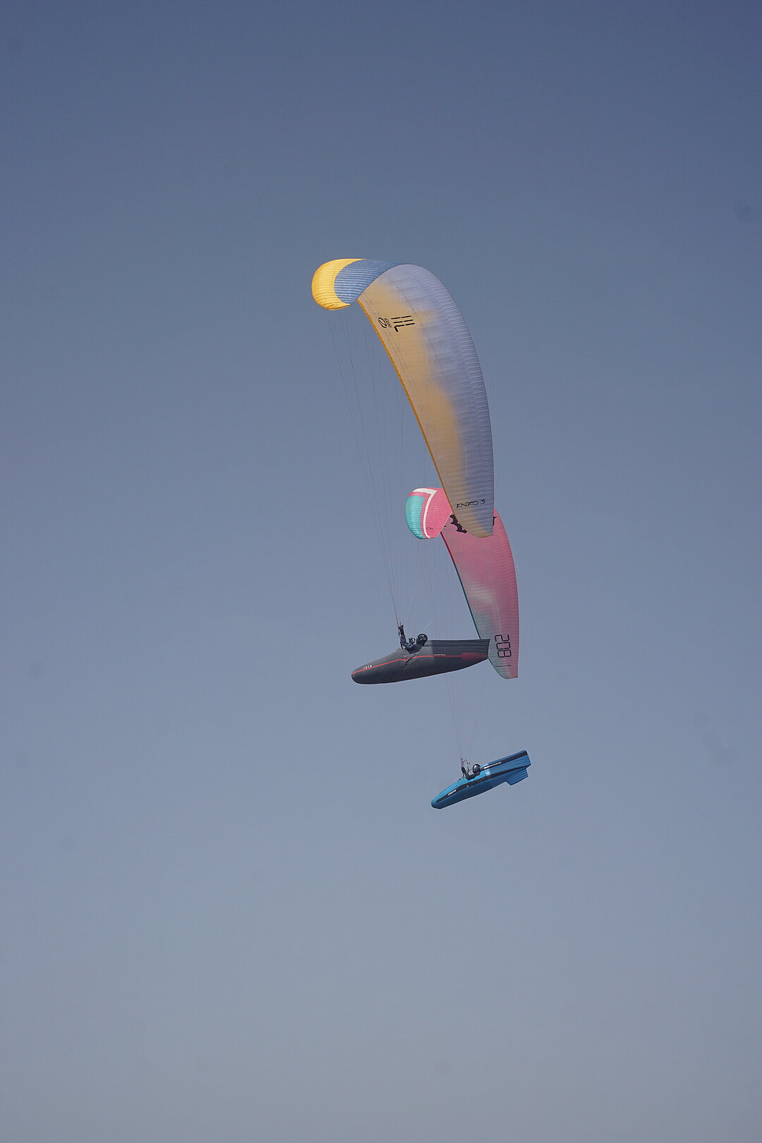 Zwei Gleitschirme fliegen dicht nebeneinander vor hellem Himmel.