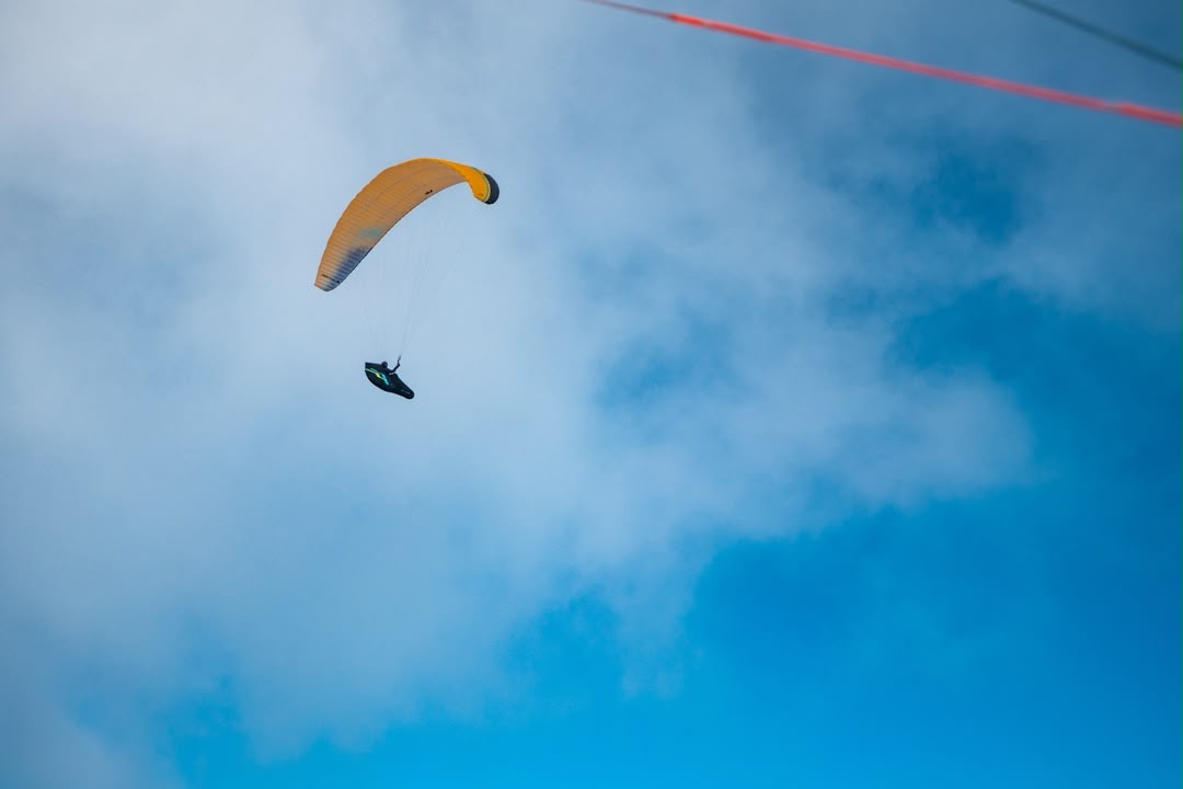 Ein Gleitschirmflieger mit gelbem Schirm schwebt vor Wolken am Himmel.