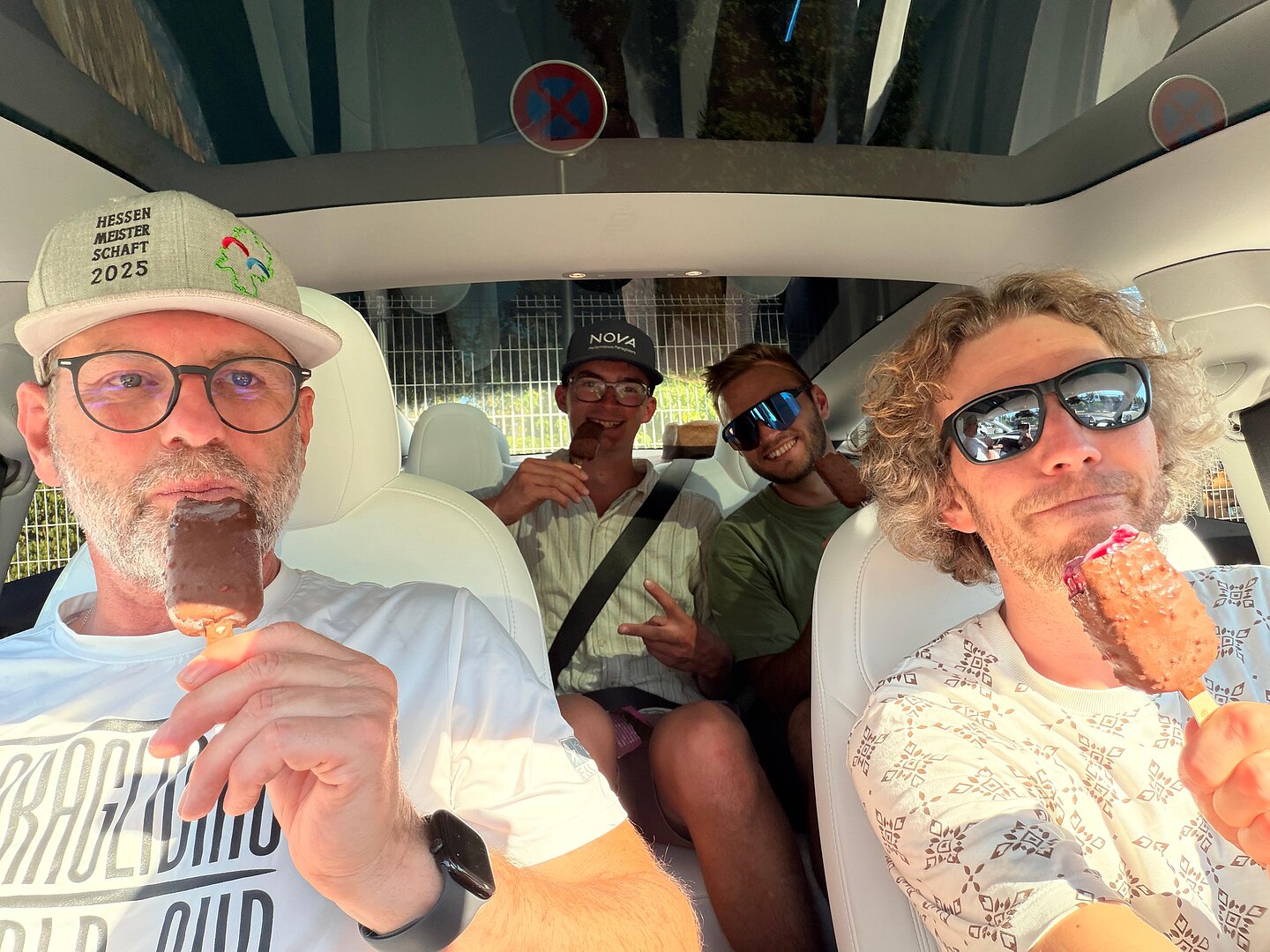 Vier Männer sitzen im Auto und essen Eis am Stiel.